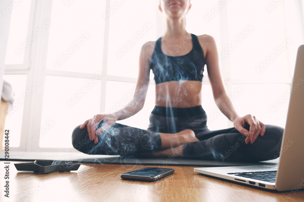 Woman sitting on yoga mat with laptop and scents Woman sitting on yoga mat with laptop and scents
