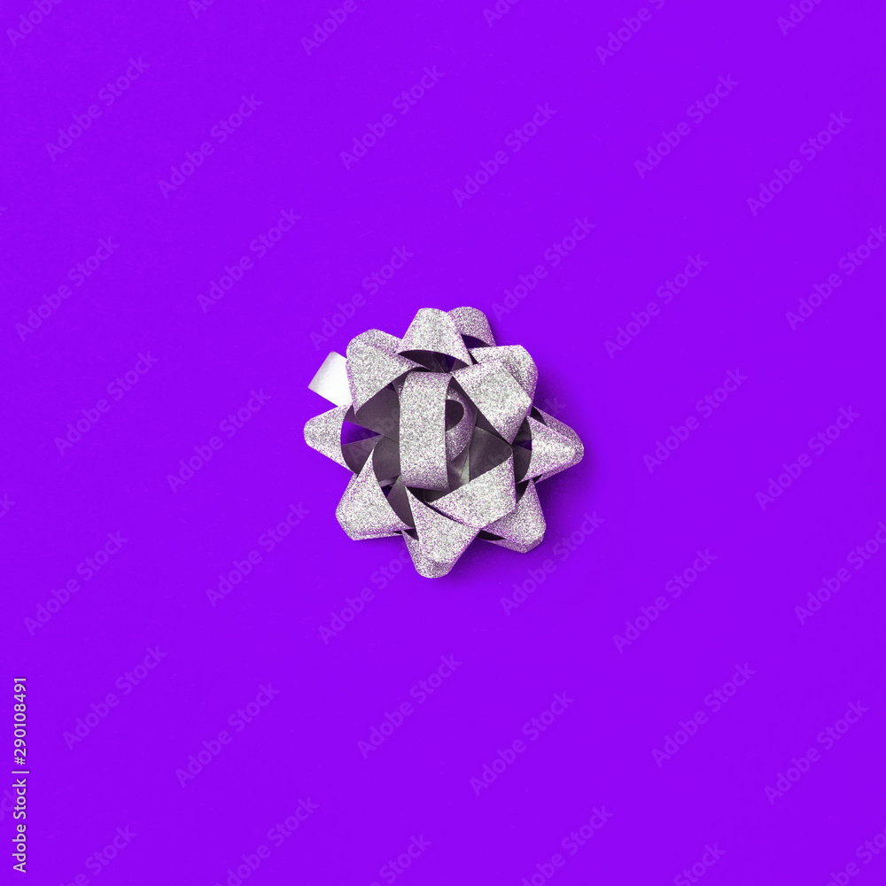 Silver bow on purple paper background. Shiny bow from ribbon. Proton purple. Color trend 2019.