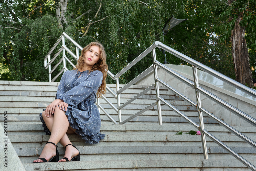 Brunette girl sitting on stairs in the city. Girl in blue dress with long hair on the street Brunette girl sitting on stairs in the city. Girl in blue dress with long hair on the street
