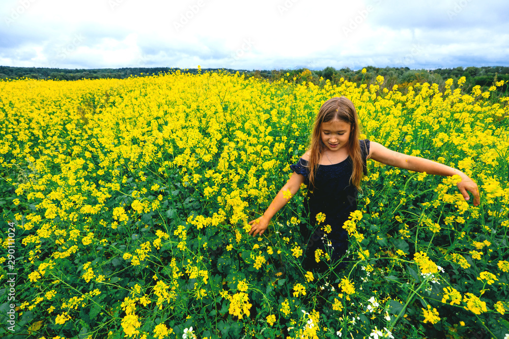 Happy girl rejoices summer walking on meadow with many yellow flowers. Young child playing outside. Summertime day activity. Happy, joyful kid outdoors. Having fun alone. Beautiful, scenic landscape Happy girl rejoices summer walking on meadow with many yellow flowers. Young child playing outside. Summertime day activity. Happy, joyful kid outdoors. Having fun alone. Beautiful, scenic landscape