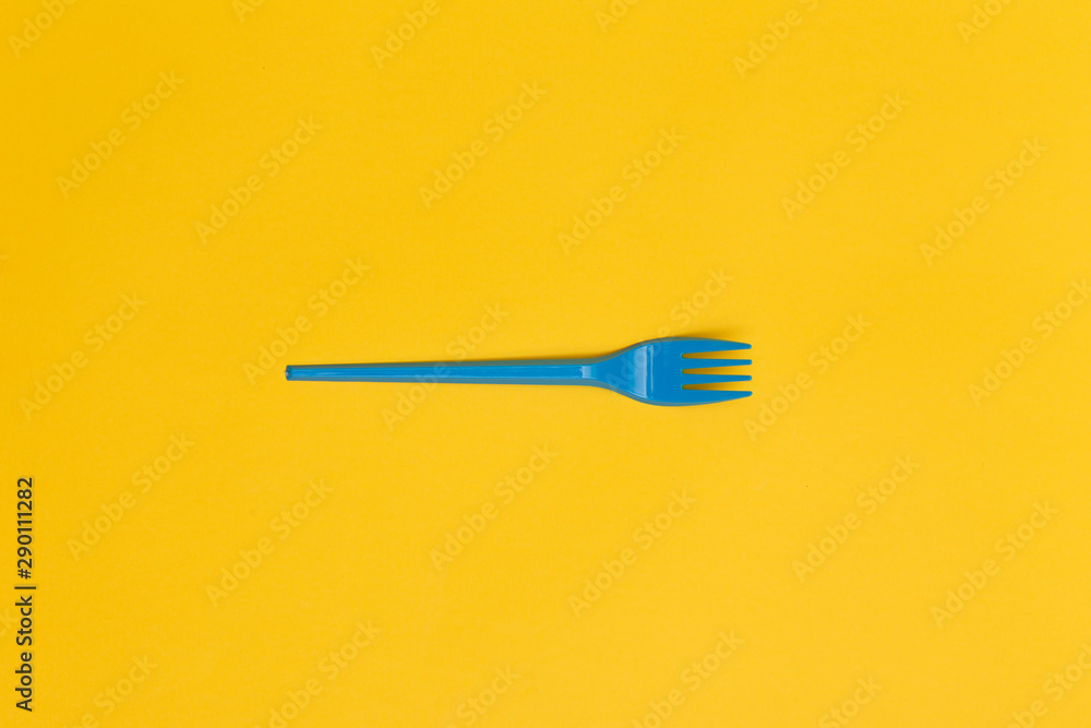 Single blue disposable fork over a yellow background. Single blue disposable fork over a yellow background.