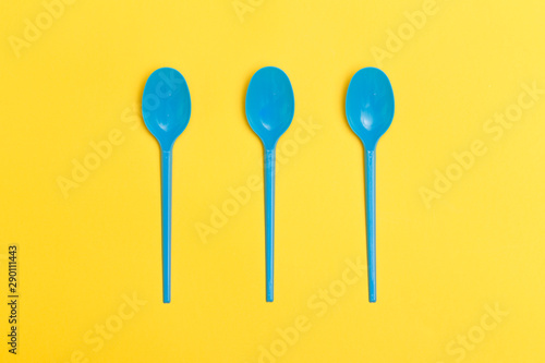 Three blue disposable plastic spoons over a yellow background.