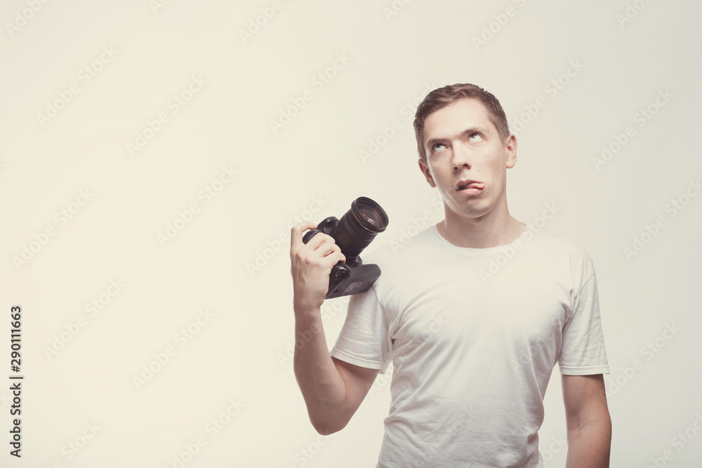 Dizzy Emotional Man with camera isolated on light background. Young man holding camera with strabismus. Lifestyle, travel and technology concept. Glad boy in white t-shirt doing antics Dizzy Emotional Man with camera isolated on light background. Young man holding camera with strabismus. Lifestyle, travel and technology concept. Glad boy in white t-shirt doing antics