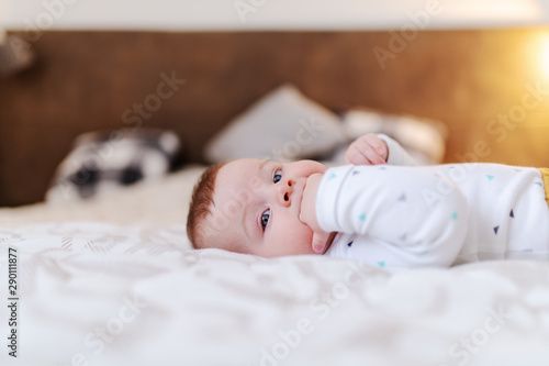 Photos Side view of adorable caucasian baby boy six months old lying in bed and sucking fingers