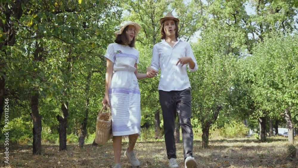 Cute couple walking in the park or garden holding hands, talking and smiling. The man with long hair and pretty woman spending time together outdoors. Retro style. Cute couple walking in the park or garden holding hands, talking and smiling. The man with long hair and pretty woman spending time together outdoors. Retro style.