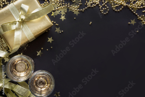 Luxury golden gift box with two glass champagne on shine black background. Christmas party. Flat lay. View from above. Xmas.