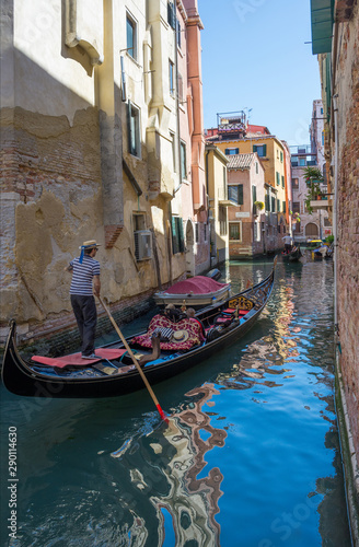 Narrow canal in Venice, Italy, with gondolas and historic houses, in a beautiful sunny day.