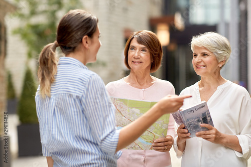 tourism, travel and friendship concept - female passerby showing direction to senior women with city guide and map on tallinn street