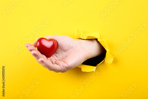 Hand holding red heart from yellow torn paper