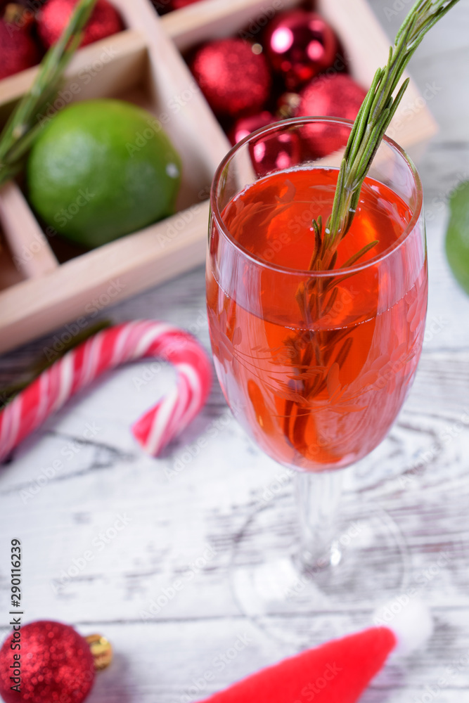 Red alcoholic drink in a tall glass surrounded by Christmas attributes against white wooden background Red alcoholic drink in a tall glass surrounded by Christmas attributes against white wooden background
