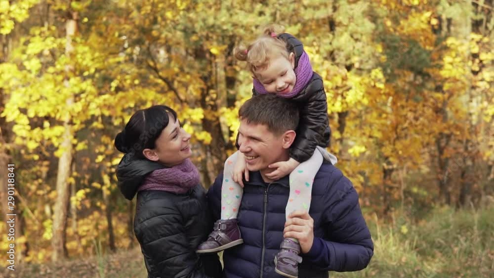 Happy family in autumn park. Child on back of father. Young family having fun outdoors Happy family in autumn park. Child on back of father. Young family having fun outdoors