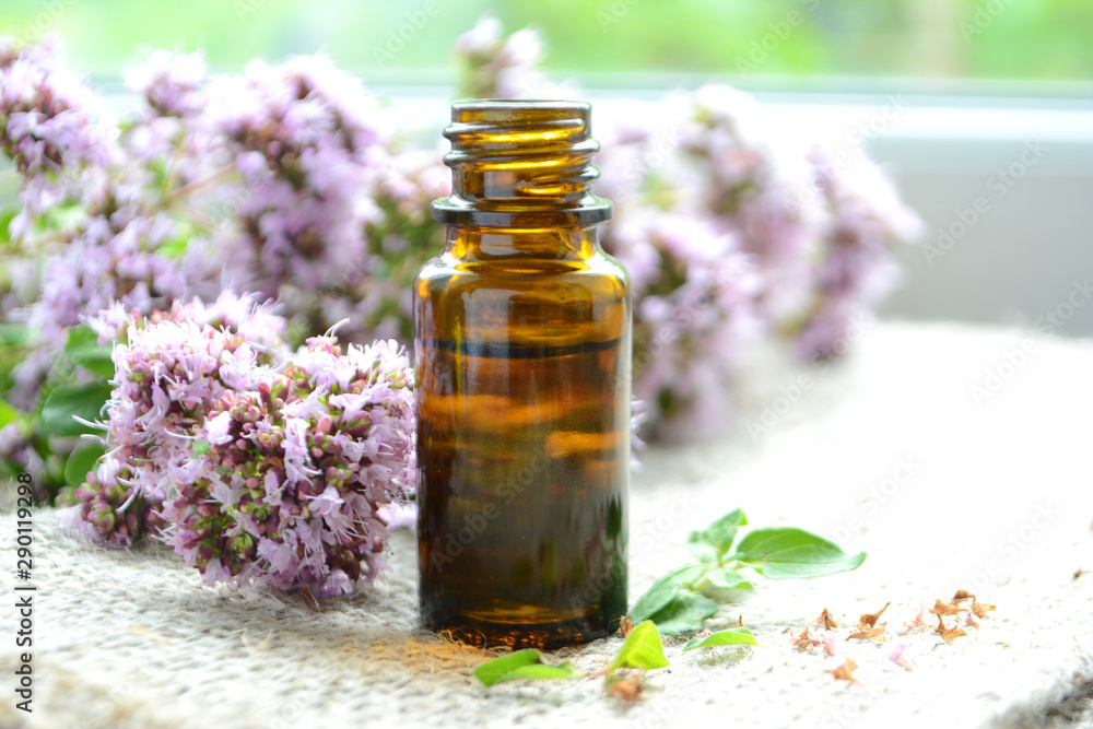 Essential oil of oregano in a bottle and fresh flowers on a wooden table Natural cosmetics and aromatherapy Essential oil of oregano in a bottle and fresh flowers on a wooden table Natural cosmetics and aromatherapy