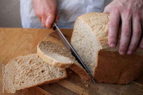 man holds a large kitchen knife in his hand and cuts with it freshly baked, fragrant, crisp rye bread, a symbol of food, copy space