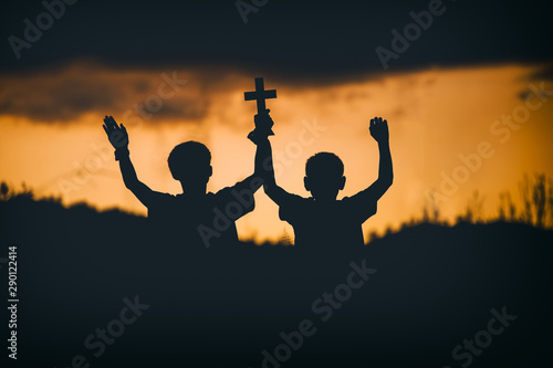 Two young christian holding cross on sky for worship and pray with sunset background,christian silhouette concept.