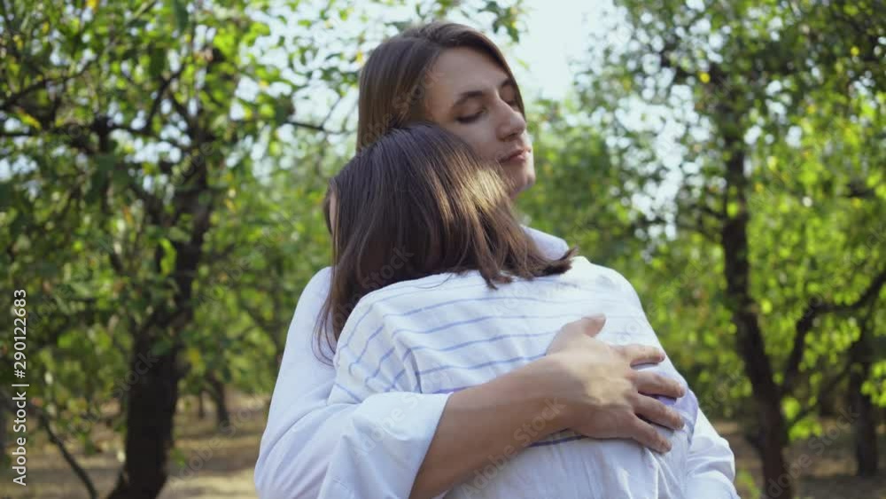 Happy young couple hugging and smiling happily while standing in park or garden. Leisure outdoors, connecting with nature. Camera moving around. Happy young couple hugging and smiling happily while standing in park or garden. Leisure outdoors, connecting with nature. Camera moving around.