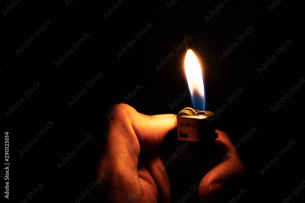 Hand holding burning gas lighters on dark background, Portable device used to create a flame, Close up Hand holding burning gas lighters on dark background, Portable device used to create a flame, Close up
