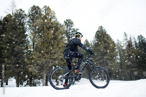 Side view of mountain biker riding in snow outdoors in winter nature.