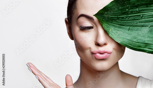 Portrait of young beautiful woman with healthy glow perfect smooth skin holds green tropical leaf. Model with natural nude make up. Gray background.