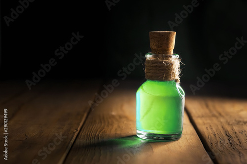 Potion in magic bottle on black and wooden background. Copy space. Selective focus