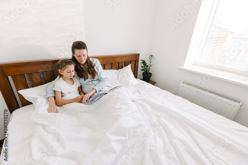Mother and child reading a book in bed in the mourning