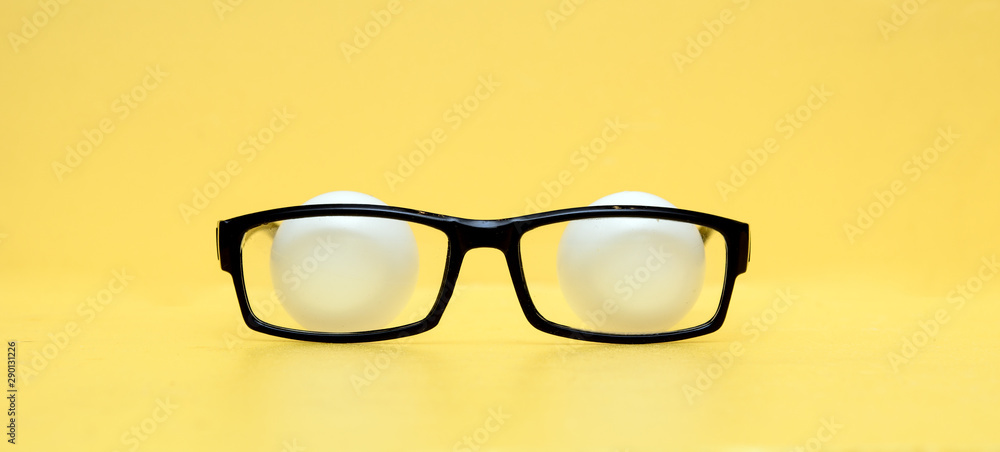 On a yellow background, glasses in a black frame. Behind the glasses are tennis balls resembling eyes. The concept is covert observation. Secret Services On a yellow background, glasses in a black frame. Behind the glasses are tennis balls resembling eyes. The concept is covert observation. Secret Services