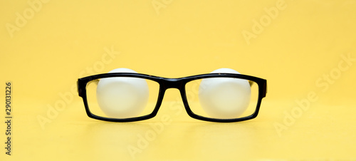 On a yellow background, glasses in a black frame. Behind the glasses are tennis balls resembling eyes. The concept is covert observation. Secret Services