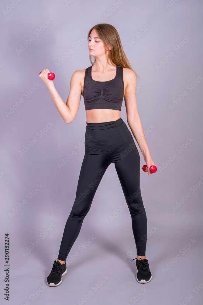 Young slim girl is doing exercises with dumbbells on a gray background. Young slim girl is doing exercises with dumbbells on a gray background.