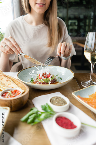 Beautiful young woman lunches in the restaurant. Tartar and a variety of dishes on the table. Italian cuisine