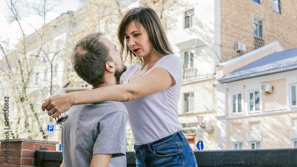 A happy loving couple look into each other's eyes in the city street. A young woman embraces a man, putting her hands on his shoulders.