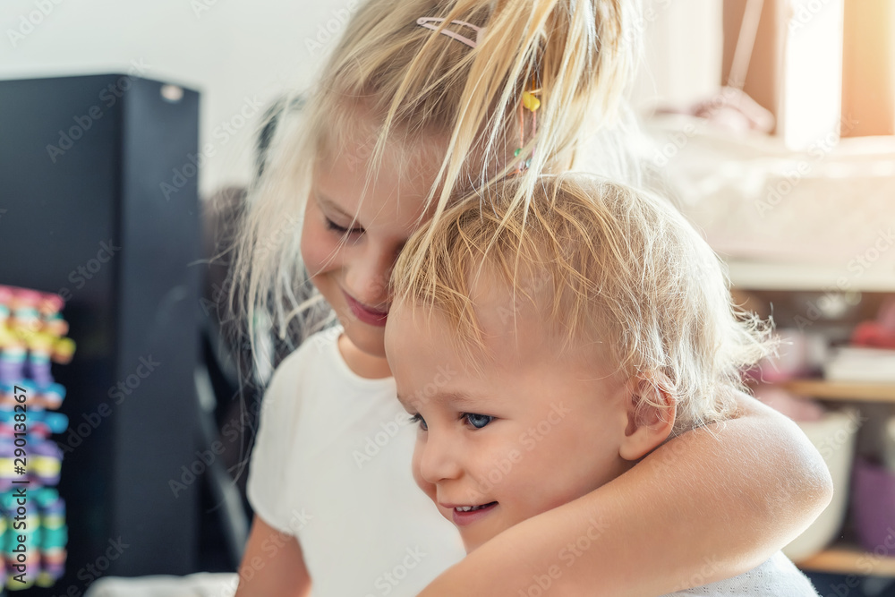 Cute adorable blond caucaian little sister hugging her toddler brother.couple of cheerful sibling playing indoor. Cute girl and baby boy enjoy relaxing at home. World kindness day