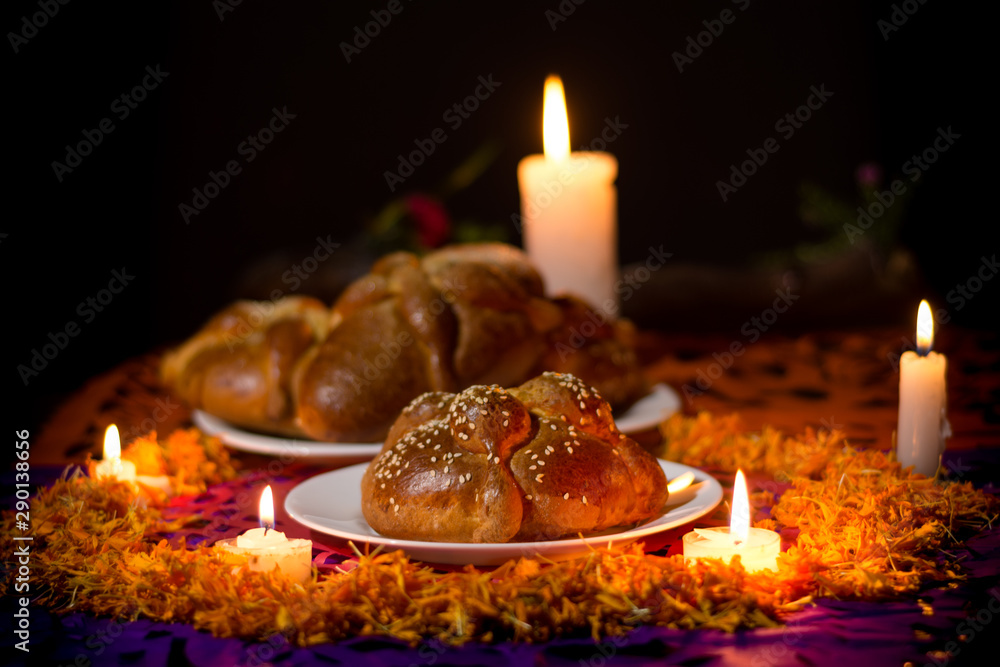 Obraz premium Pan de Muerto traditional recipe from Mexico, adorned with candles and cempasuchil flower petals, in the diffuse background, commemorating the Day of the Dead.