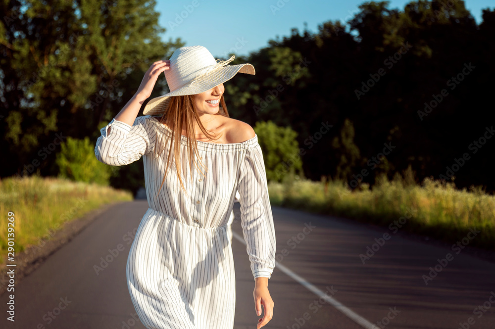 Brown-haired young girl in white walking along rural road lit by sunset sun
