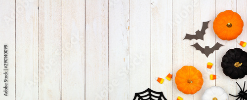 Halloween corner border banner with black, orange and white decor and candy over a white wood background. Top view with copy space.