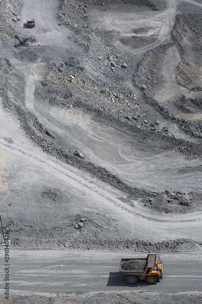 Top view, open pit work. Large quarry dump trucks take out rock on road. Grey stones background