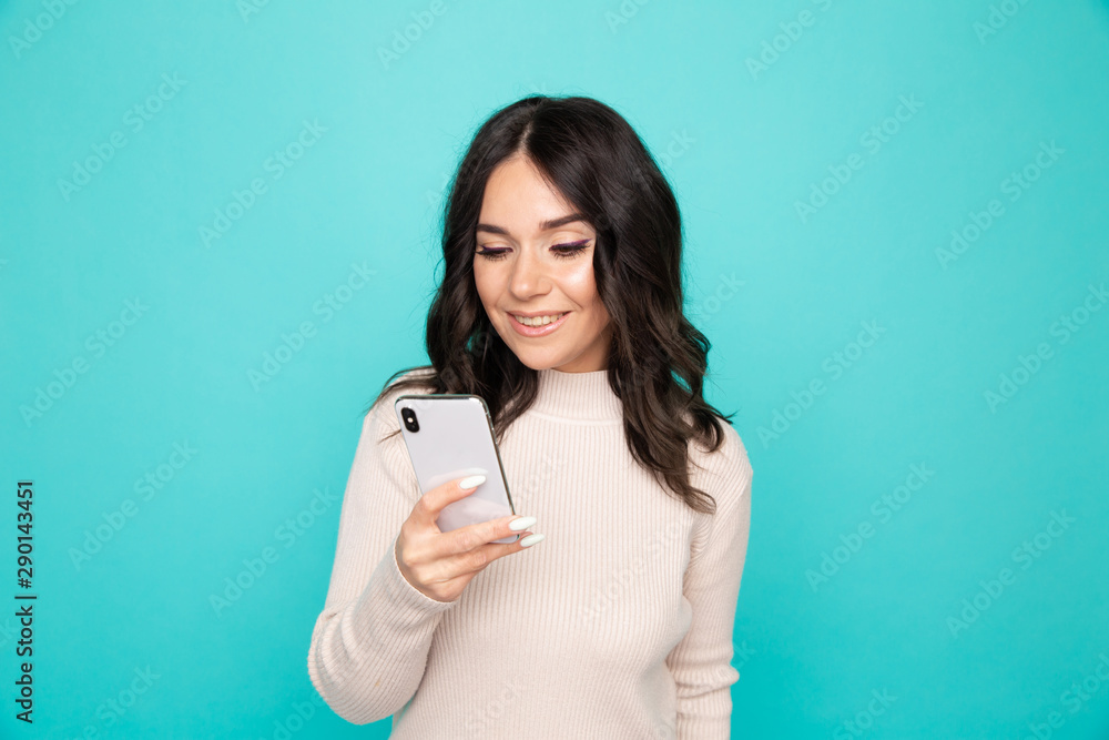 Beautiful curly hair female holding cellphone standing on the blue background Beautiful curly hair female holding cellphone standing on the blue background