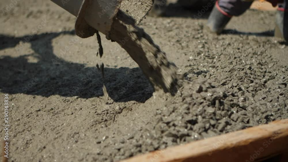 Close up shot of wet cement pouring out from cement truck shoot at a construction site as workers spread it out with shovels during afternoon. Close up shot of wet cement pouring out from cement truck shoot at a construction site as workers spread it out with shovels during afternoon.