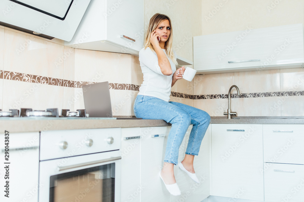 Young woman sitting on the kitchen table speak by phone, worry face. Young woman sitting on the kitchen table speak by phone, worry face.