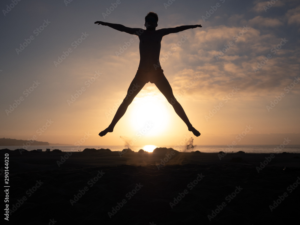 Silhouette male jumps on the beach against sunrise