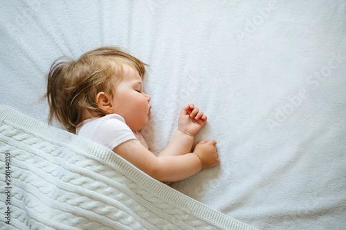 Cute little baby sleeping peacefully on bed at home covered with blanket. Child daytime sleeping schedule