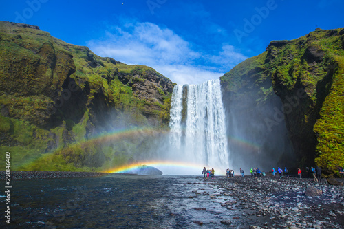 Skogafoss a summer afternoon with a rainbow and tourists under the waterfall. Iceland