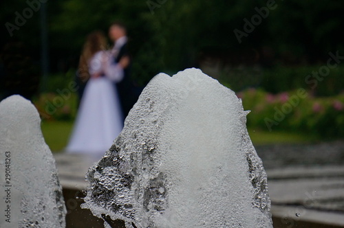 Fountain in the park, a stream of water. The bride and groom kiss.