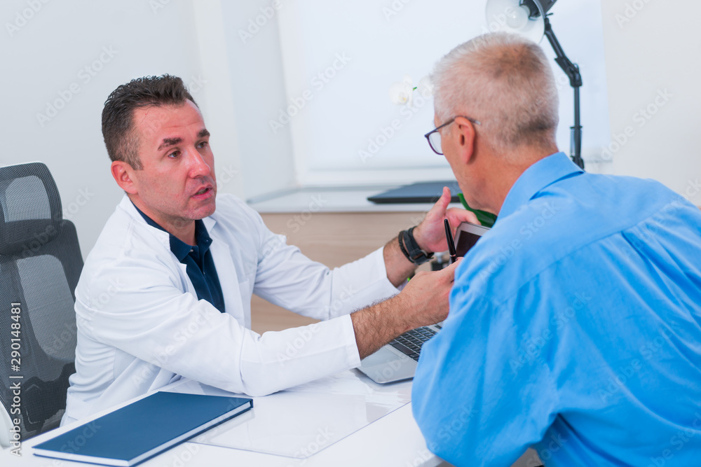 Middle aged doctor is showing his older patient ( senior ) his blood reading results on his laptop while sitting in his office. Middle aged doctor is showing his older patient ( senior ) his blood reading results on his laptop while sitting in his office.