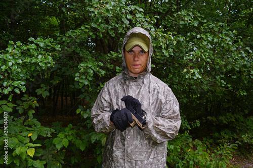 A young man in camouflage with a gun on a background of green leaves.