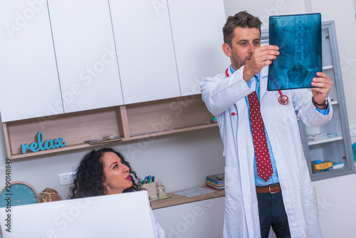 Male Doctor in his mid 40's reading an x-ray image ( radiography ) from a patient hip region ( coxa ) while standing in a hospital radiology department and discussing the result with a nurse.. photo