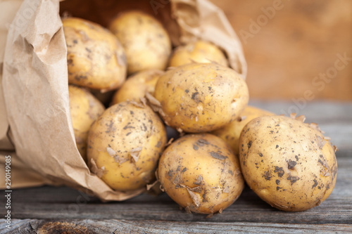 Raw potato. Fresh new potatoes in kraft paper bag on wooden background