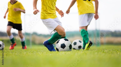 Soccer camp for kids. Boys practice dribbling in a field. Players develop good soccer dribbling skills. Children in yellow shirts training with balls. Soccer slalom drills on pitch