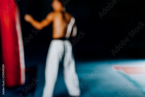 Blurred view of muscular man kick boxing with red punching bag at gym. Blurred image