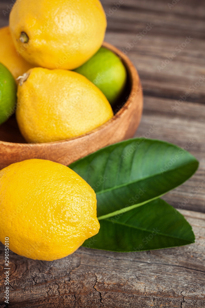 Juicy ripe citrus on old wooden background. Fresh lemons and limes in a bowl