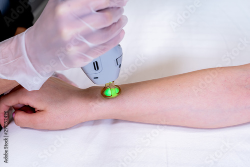 Close up of arm laser hair removal session with beauty technician and female patient, epilating after shaving, in a cosmetology skin clinic.