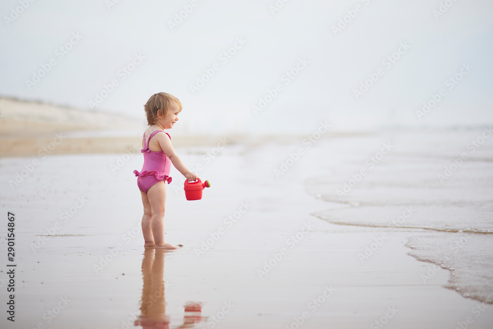 girl playing with red watering can on the ocean beach girl playing with red watering can on the ocean beach